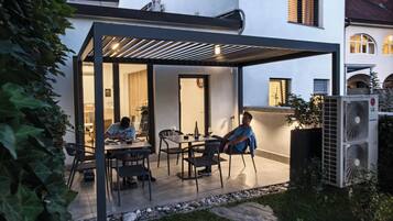 A modern outdoor patio with a pergola, seating, and a person working at a table.