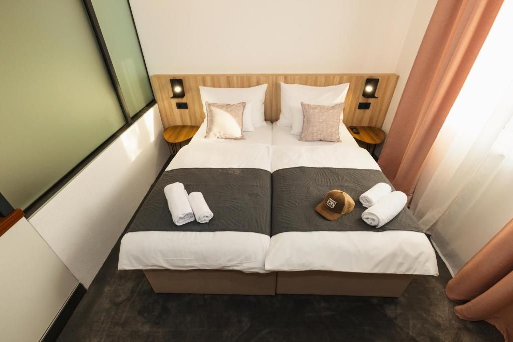 Ein Doppelbett mit zwei Kissen, einem Holz-Kopfteil, Nachttischlampen und gerollten Handtüchern.