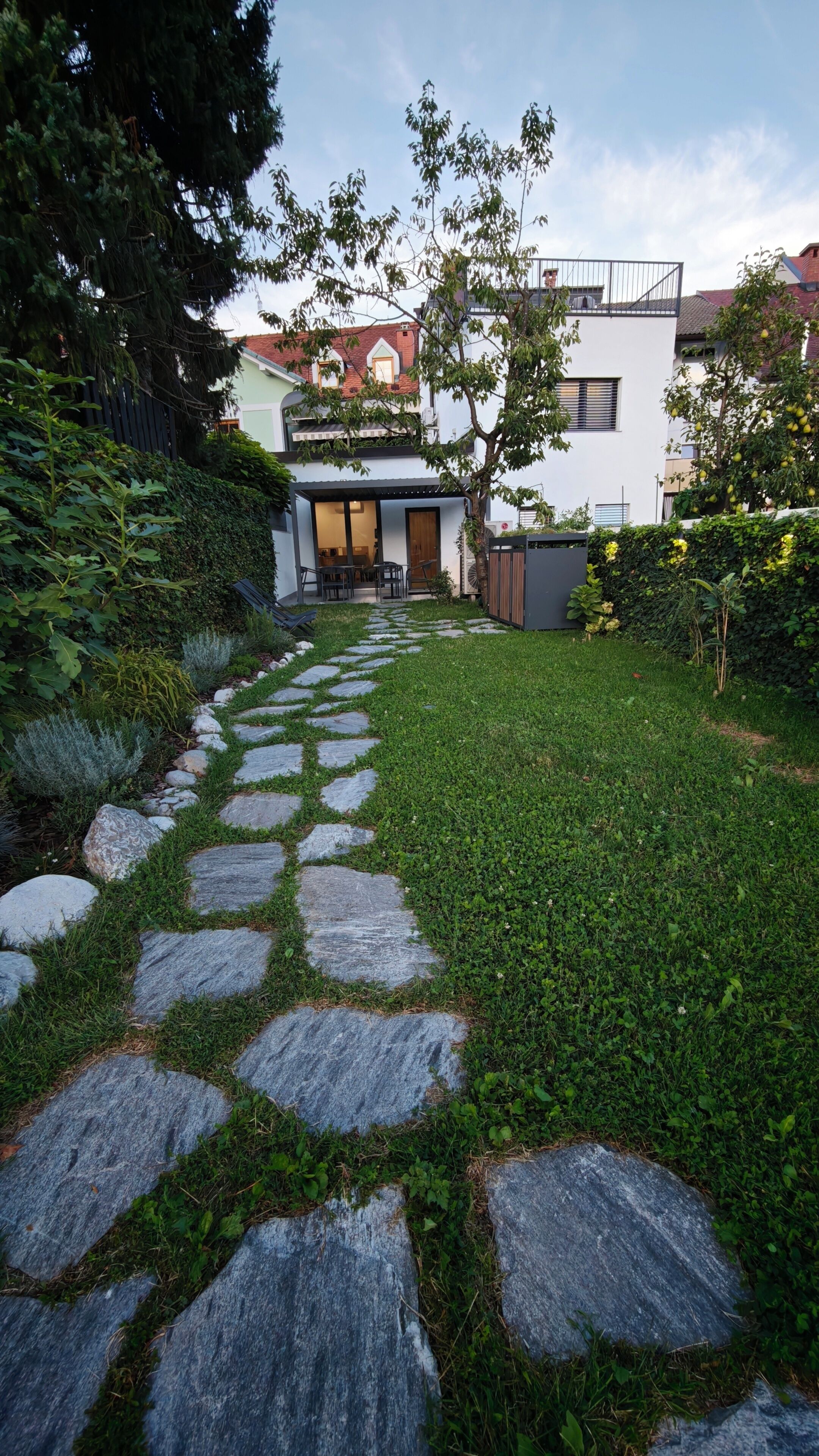 A stone pathway leading to a modern house with a visible entrance and a small patio area.