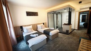 Een hotelkamer met twee bedden, een badkamer met een douchecabine van glas en een houten tafel.