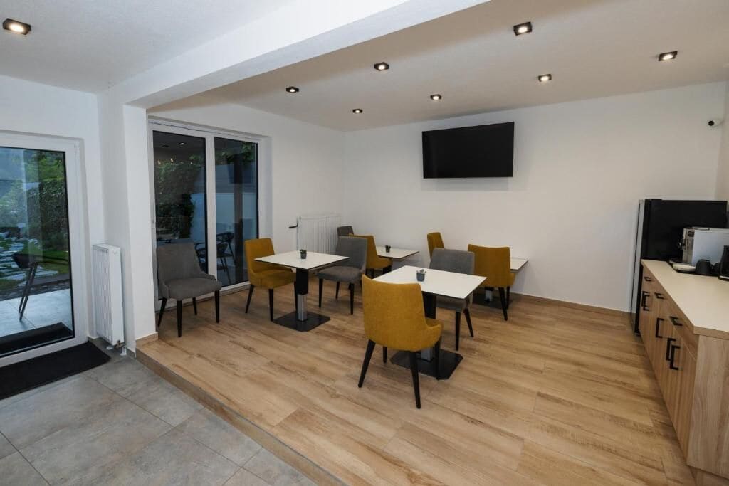 A modern dining area with tables and chairs, a flat-screen TV mounted on the wall, and a wooden floor.