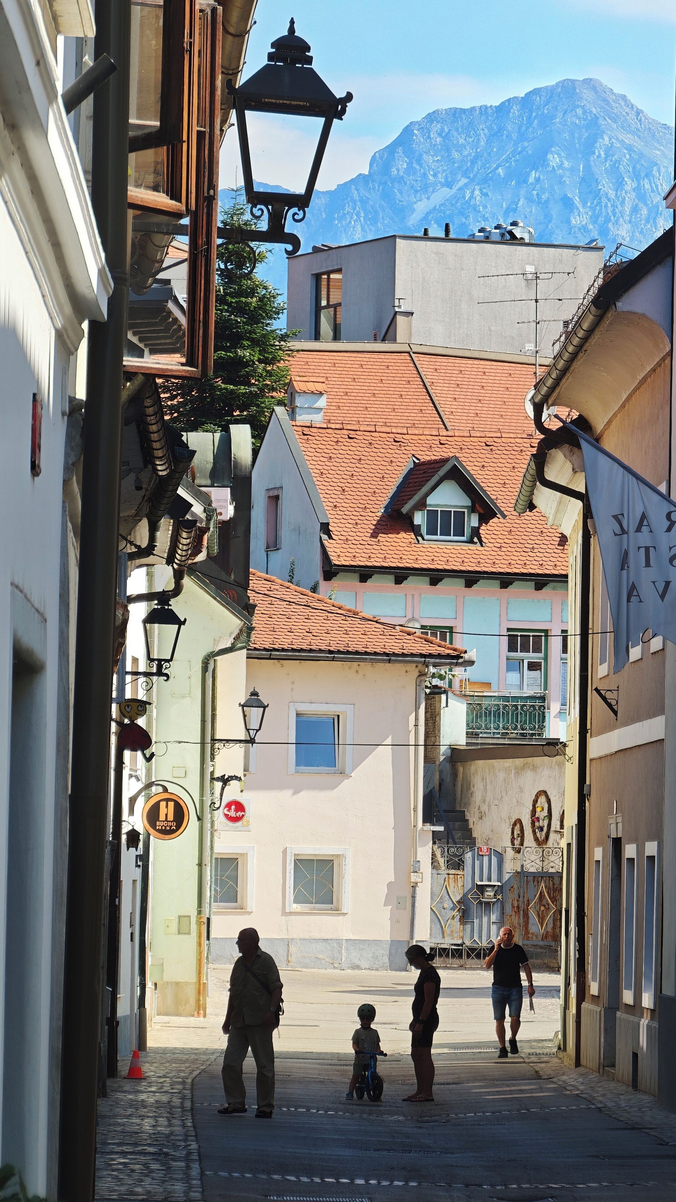 Una calle estrecha con edificios tradicionales, una montaña al fondo y algunos peatones.