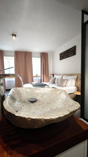 Un baño moderno con un lavamanos de piedra grande, una ducha y una cama con cabecera de madera.