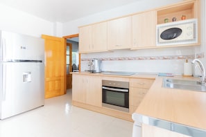 Una cocina con armarios de madera, horno empotrado, microondas y pileta.