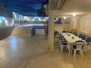 Un comedor con mesa y sillas, una escalera y una zona de piscina con luces.