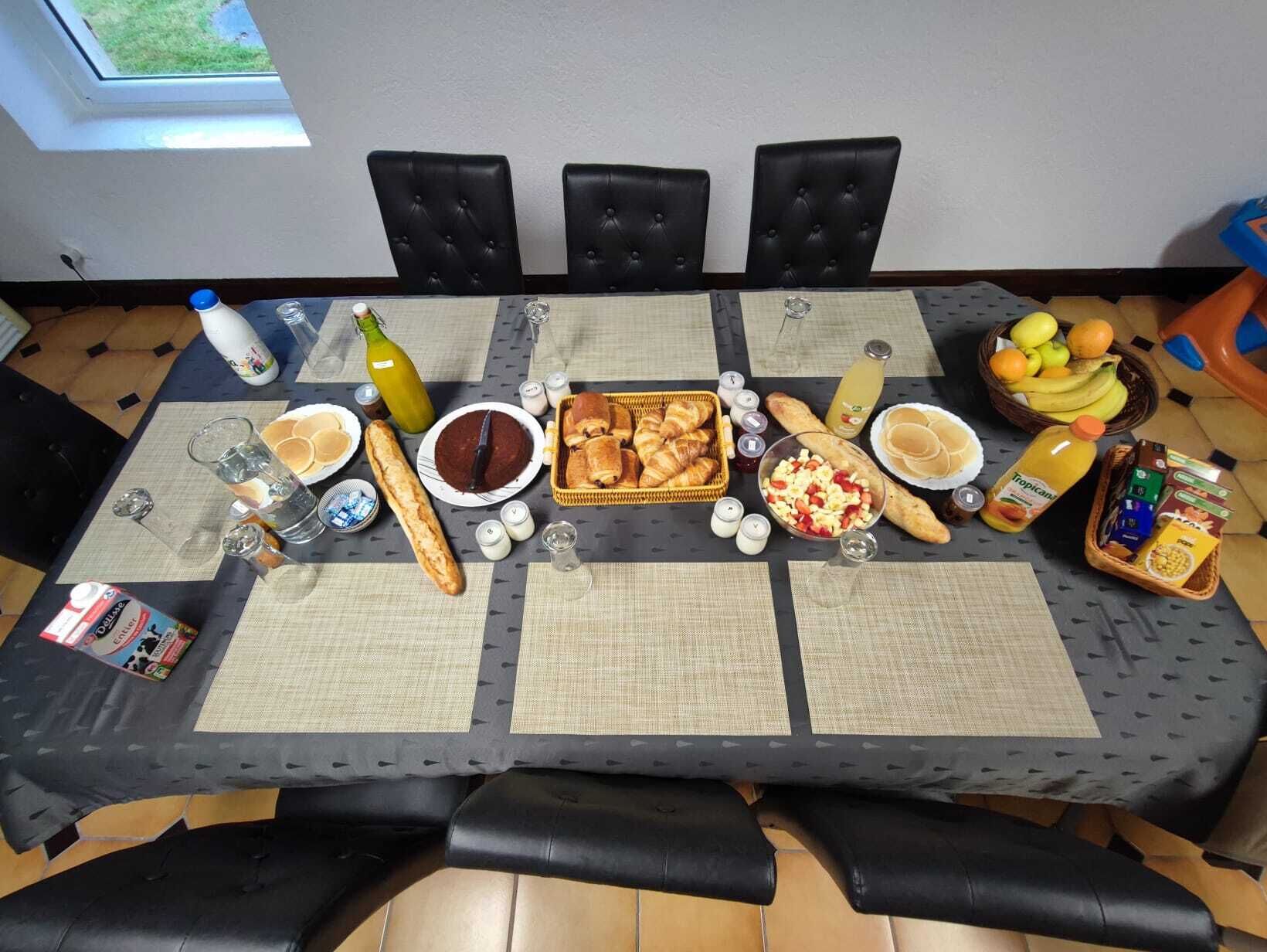 Une table à manger dressée avec divers plats et boissons, entourée de chaises noires recouvertes de tissu.