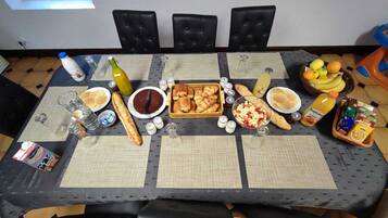 Une table à manger dressée avec divers plats et boissons, entourée de chaises noires recouvertes de tissu.