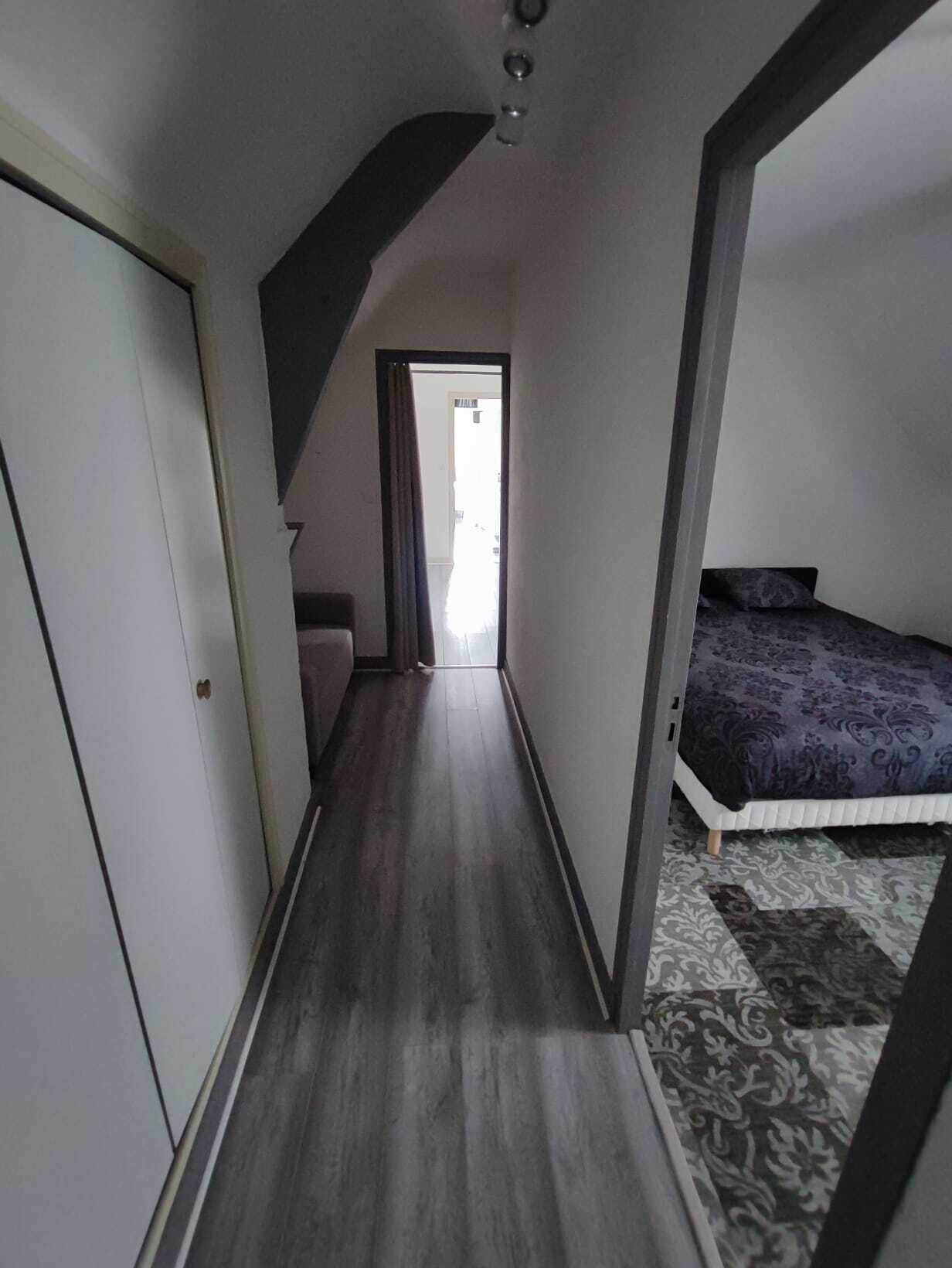 Corredor estreito que dá para um quarto, com uma cama e uma porta à esquerda.