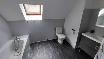 Une salle de bain moderne dotée d’une lucarne, d’une baignoire, de toilettes et d’un meuble-lavabo.