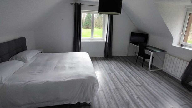A bedroom with a bed, a desk, a television, and a window with curtains. - Domaine Sylvaria - Bed and Breakfast - Figuier Room (sleeps 8) Nature/Peace and Quiet/Swimming Pool (Lassay-sur-Croisne)