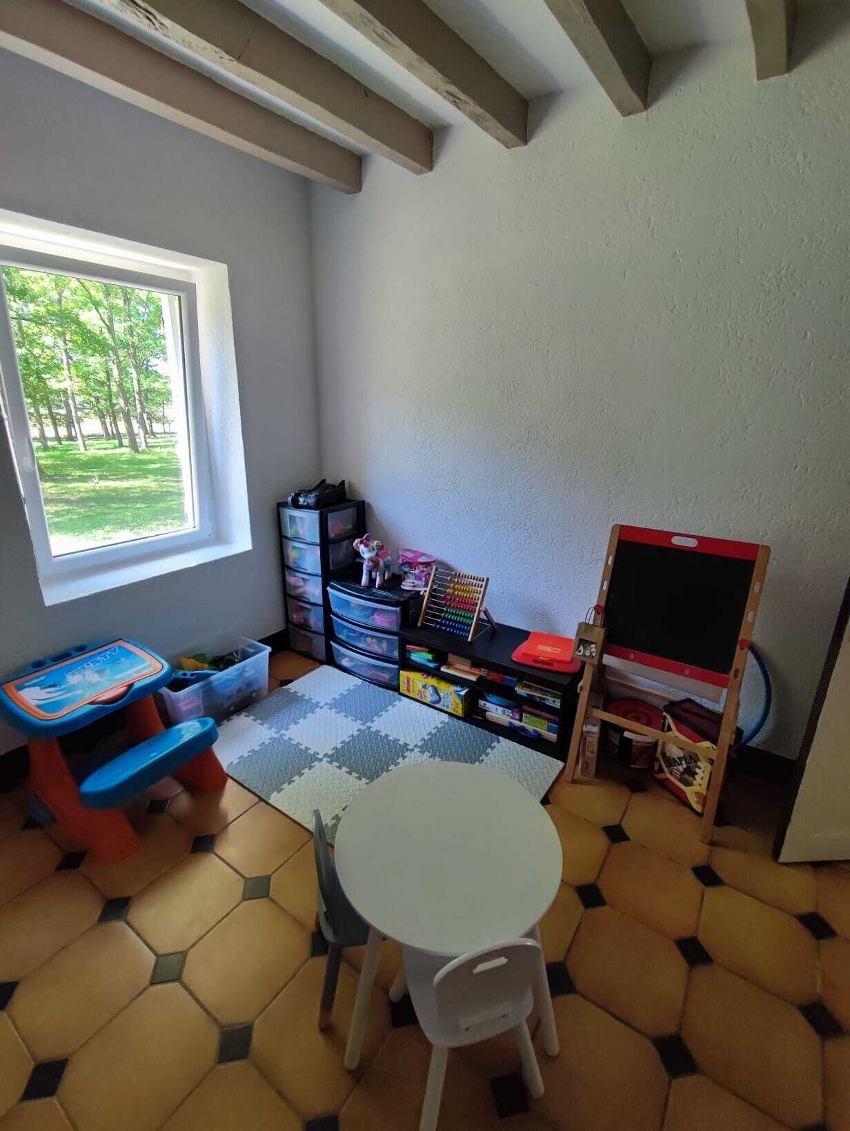 Een kinderspeelkamer met een raam, opbergkasten, een klein tafeltje en een stoel.