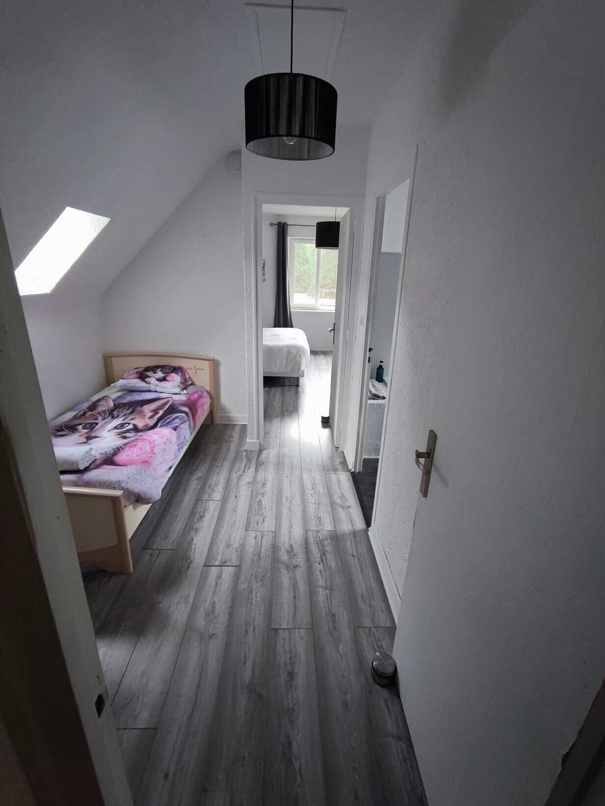 Un couloir étroit menant à une chambre dotée d’un plafond en pente et d’un puits de lumière.