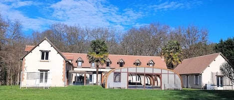 Une grande maison de plain-pied, dotée d’un vaste jardin à l’avant et surplombant un ciel d’un bleu éclatant.
