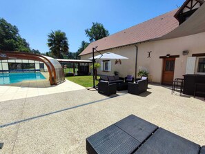 A pool area with a glass enclosure, outdoor seating, and a building with a tiled roof.