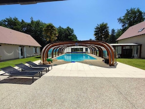 En swimmingpool med ett överbyggt område, solstolar och en byggnad med ett tak täckt av tegelpannor.