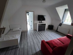 Ett sovrum med en säng, en röd soffa, en tv på ett tv-bord och ett fönster med utsikt.