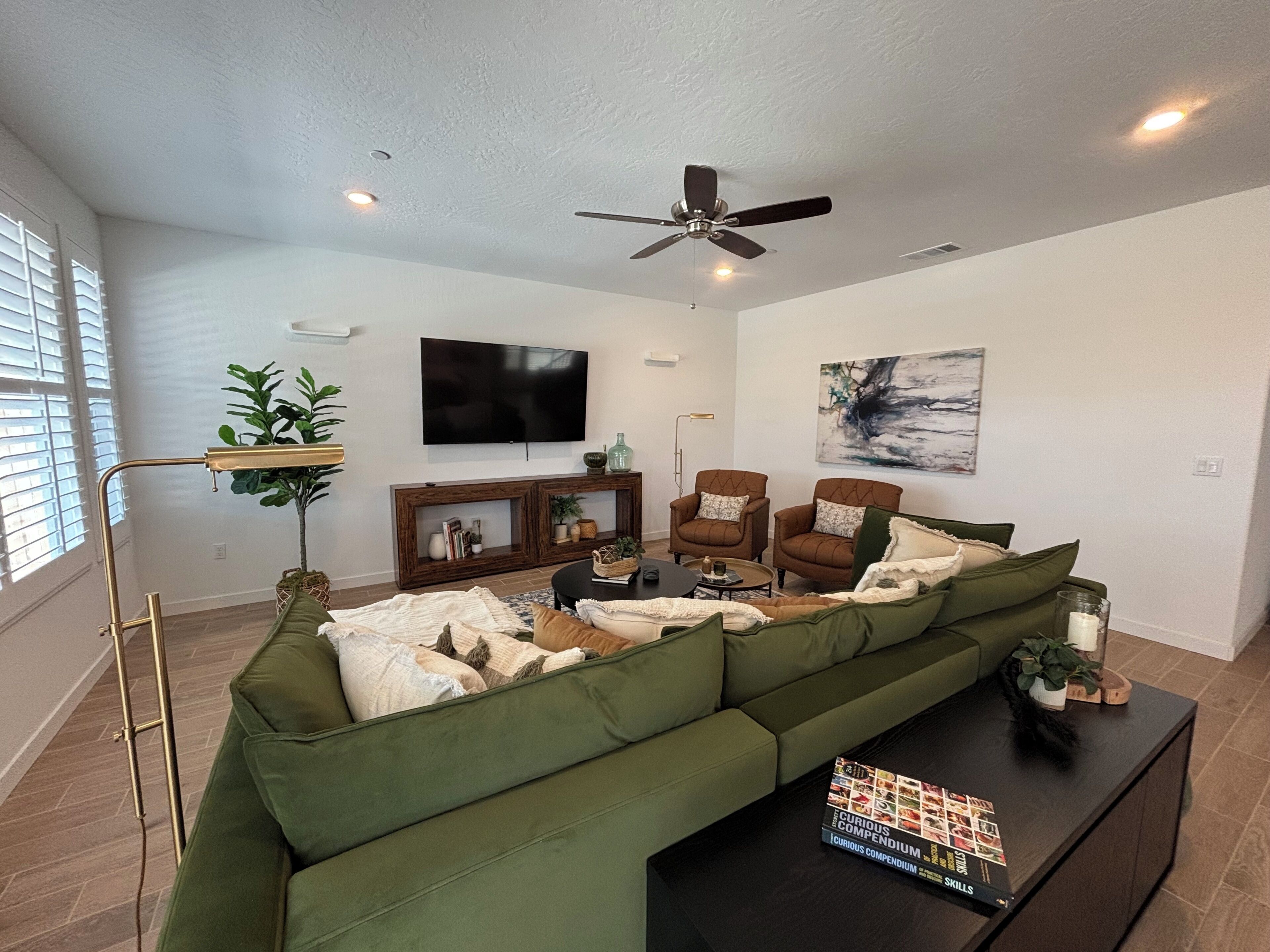 A living room with a sectional sofa, a coffee table, a TV, and a ceiling fan.
