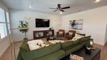 A living room with a sectional sofa, a coffee table, a TV, and a ceiling fan.