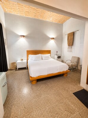 A hotel room with a wooden bed, two bedside tables, a chair, a wall-mounted towel rack, and a small heater. - A unique spot in Oaxaca's Historic District. Parks, restaurants, and museums within walking distance. (Oaxaca de Juárez)