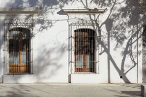 A building facade with two arched windows, each with metal bars and wooden shutters, set in a white wall with classical architectural details. - A unique spot in Oaxaca's Historic District. Parks, restaurants, and museums within walking distance. (Oaxaca de Juárez)