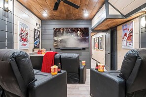 Ein modernes Wohnzimmer mit Ledersofas, einem Flachbildfernseher, Popcorn und Filmplakaten an den Wänden.