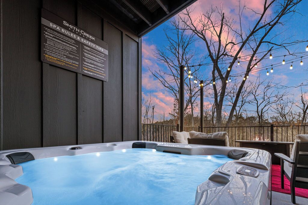 A hot tub with a view of a sunset, a sign with spa rules, and a wooden deck.