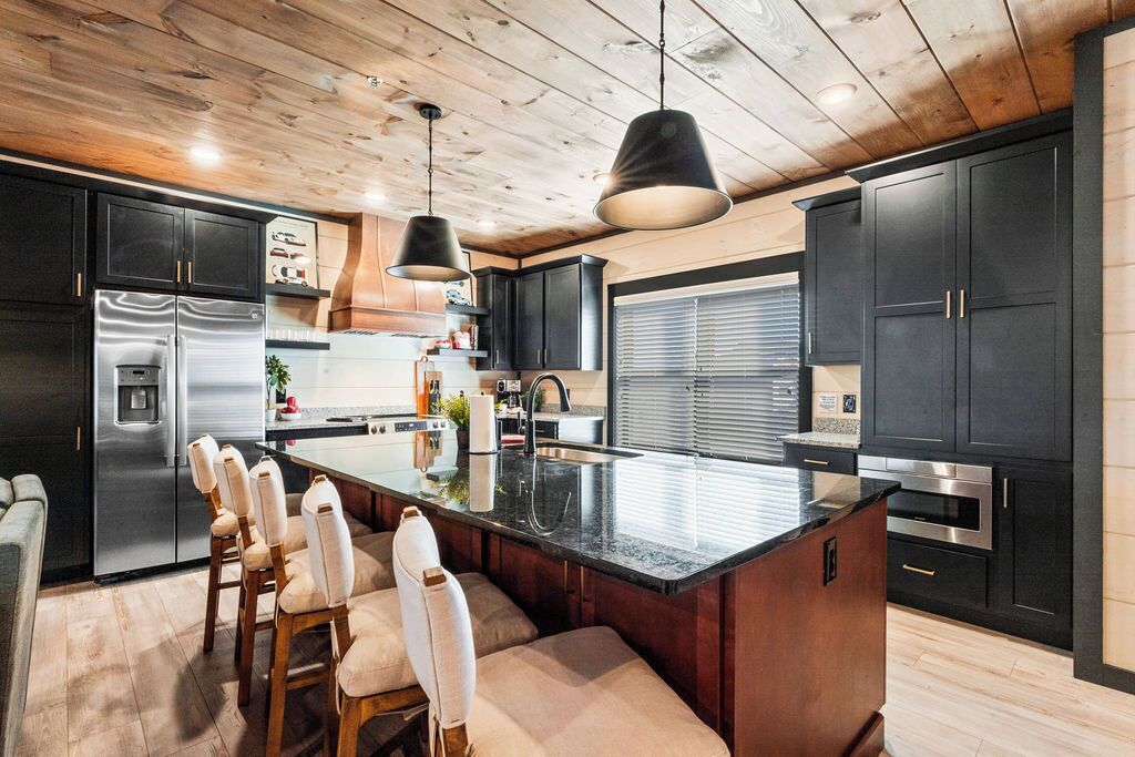 A modern kitchen with a large island, dark cabinetry, and pendant lighting.