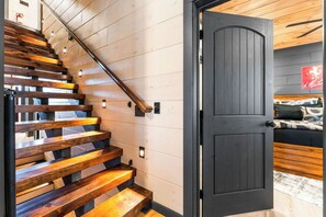 Un escalier en bois mène à une porte sombre qui donne sur une chambre.