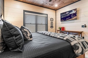 Ein Schlafzimmer mit einem großen Bett, einem an der Wand montierten Fernseher und einem Fenster mit Jalousien.