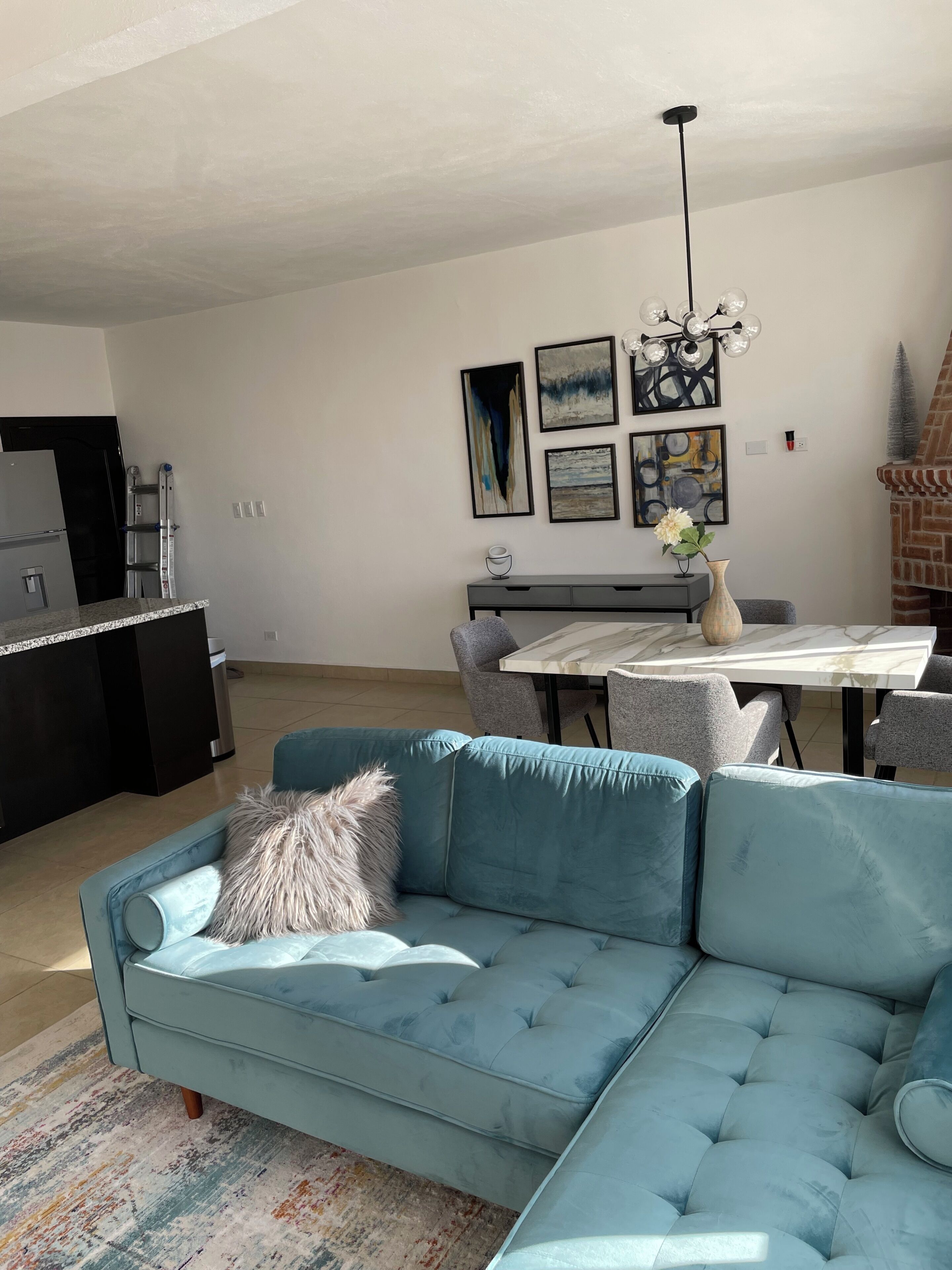 Un salon moderne comprenant un canapé d’angle, une table à manger avec des chaises et un coin cuisine avec un réfrigérateur.