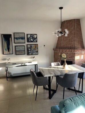 Une cuisine moderne avec une cheminée en briques, une table à manger avec des chaises et des œuvres d’art abstraites accrochées au mur.