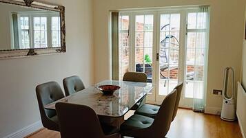 A dining area with a glass table, four chairs, a large mirror, and a view through a glass door to the outside.