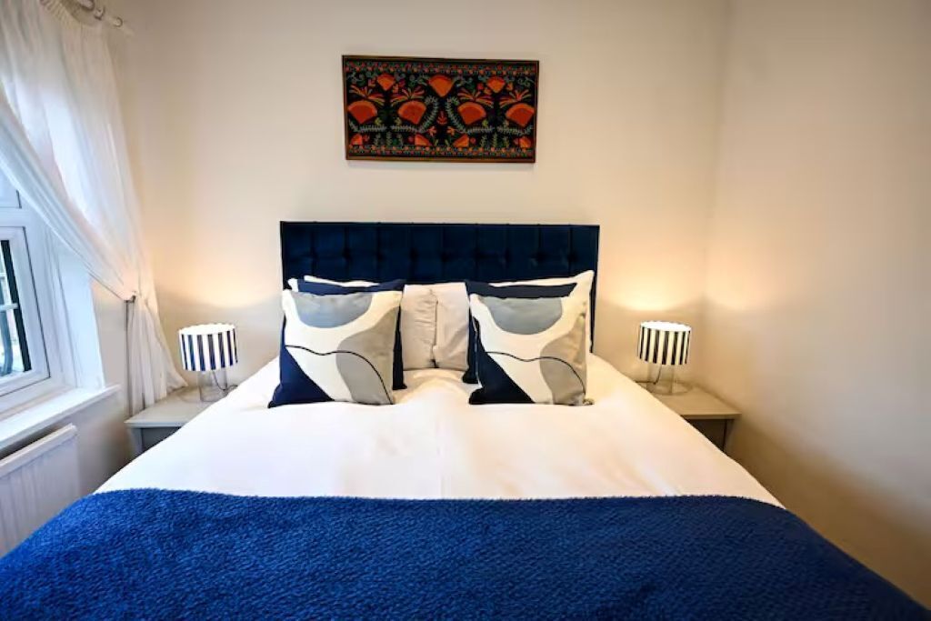 Een hotelkamer met een bed, twee bedlampen, een raam met gordijnen en een kunstwerk aan de muur.