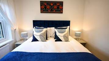 Een hotelkamer met een bed, twee bedlampen, een raam met gordijnen en een kunstwerk aan de muur.