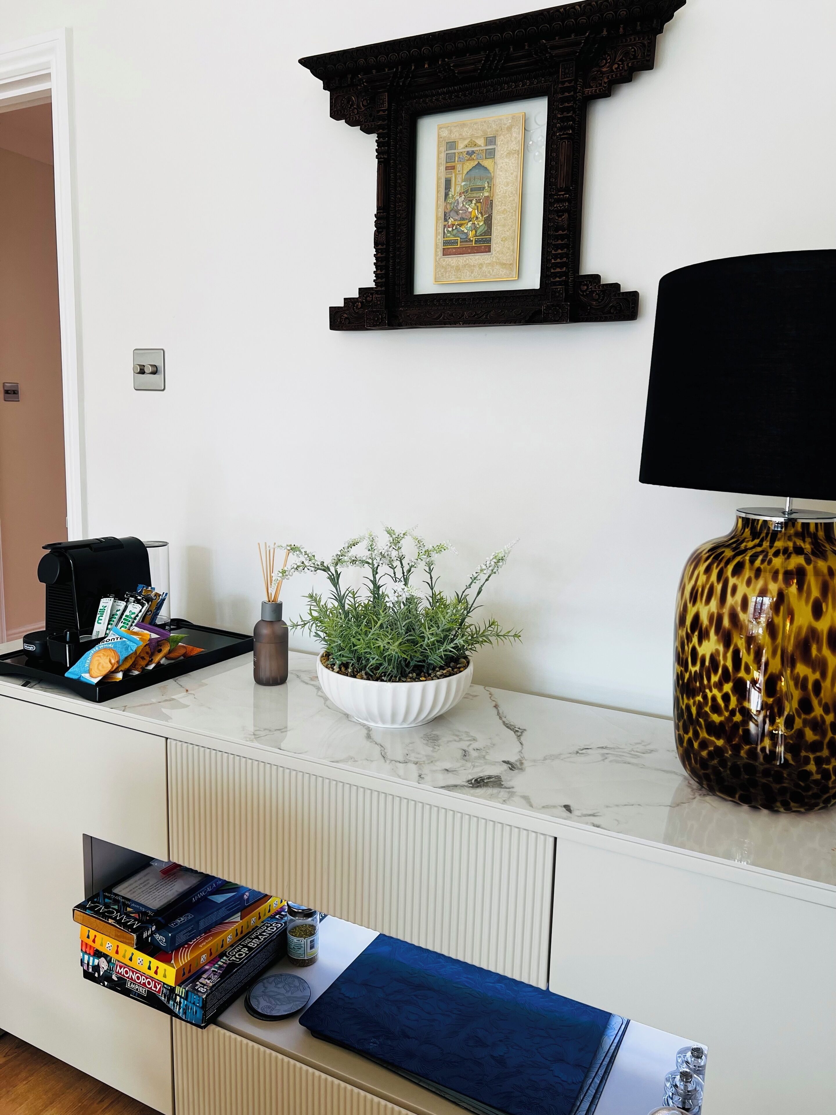 Een kamer met een witte kast, een koffieapparaat, een plant, een spel en een lamp.