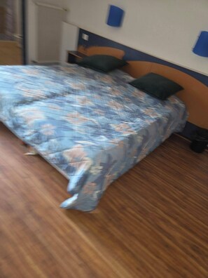 A bed with a floral bedspread, a wooden headboard, and two pillows. - Cozy 1-bedroom apartment in beautiful Fleury with AC 50m from the beach (Fleury)