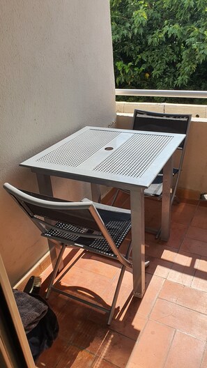 A metal table and chairs on a tiled patio with a view of greenery. - Cozy 1-bedroom apartment in beautiful Fleury with AC 50m from the beach (Fleury)