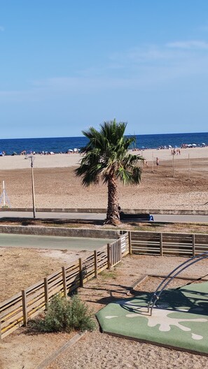 A beach with a palm tree, a volleyball net, and a playground. - Cozy 1-bedroom apartment in beautiful Fleury with AC 50m from the beach (Fleury)