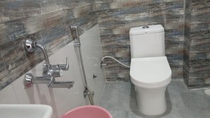 A bathroom with a white toilet, a shower with a chrome faucet, and a pink bucket.
