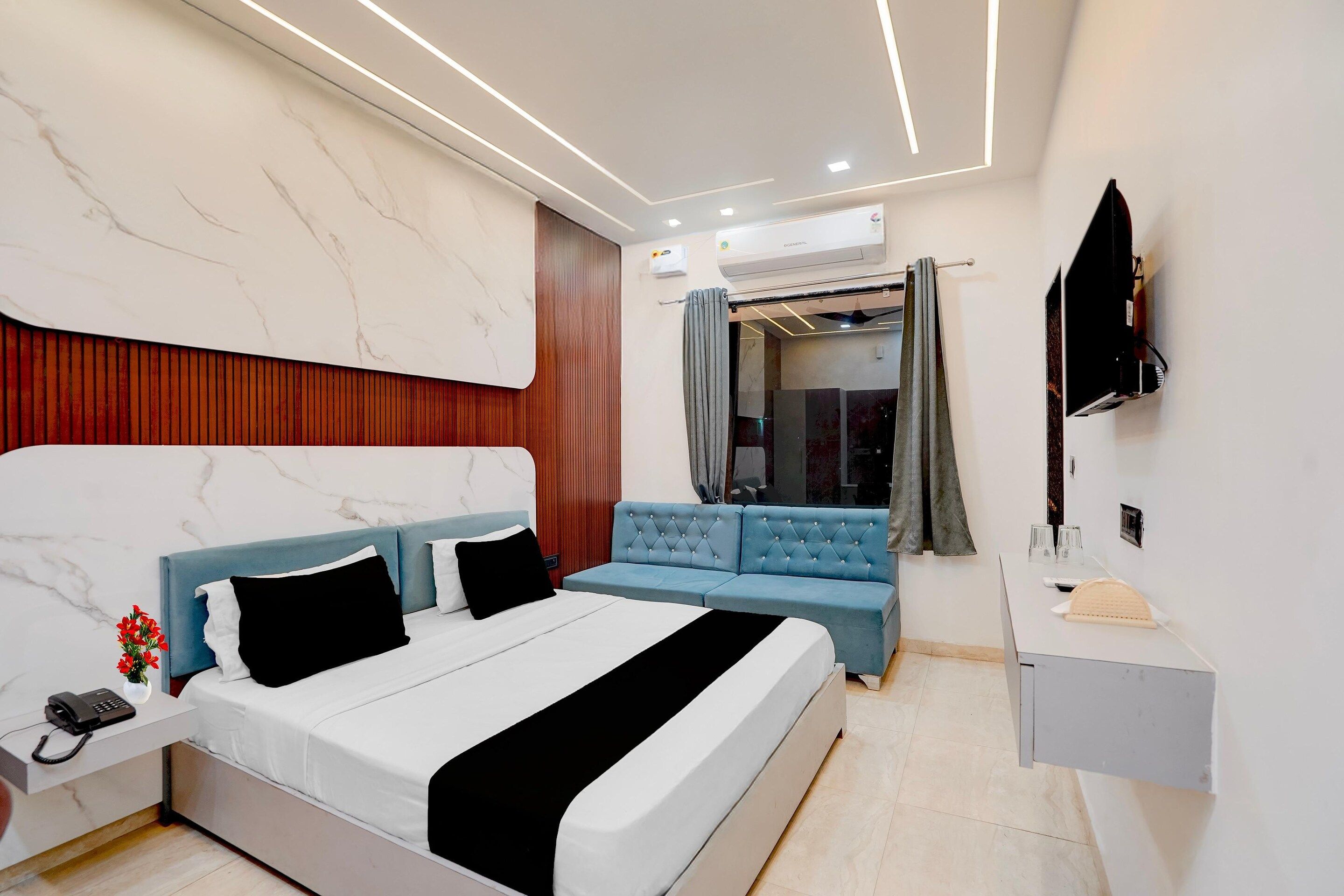 A modern bedroom with a large bed, a blue sofa, a TV, and a built-in air conditioning unit.