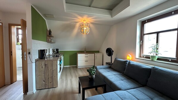 A modern living room with a grey sofa, a small coffee table, and a dining area with a kitchen counter.