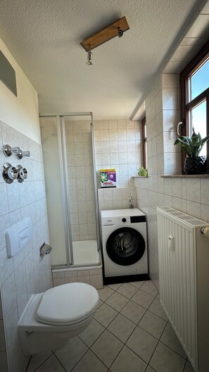 Ein kleines Badezimmer mit Toilette, Waschmaschine und Duschkabine.