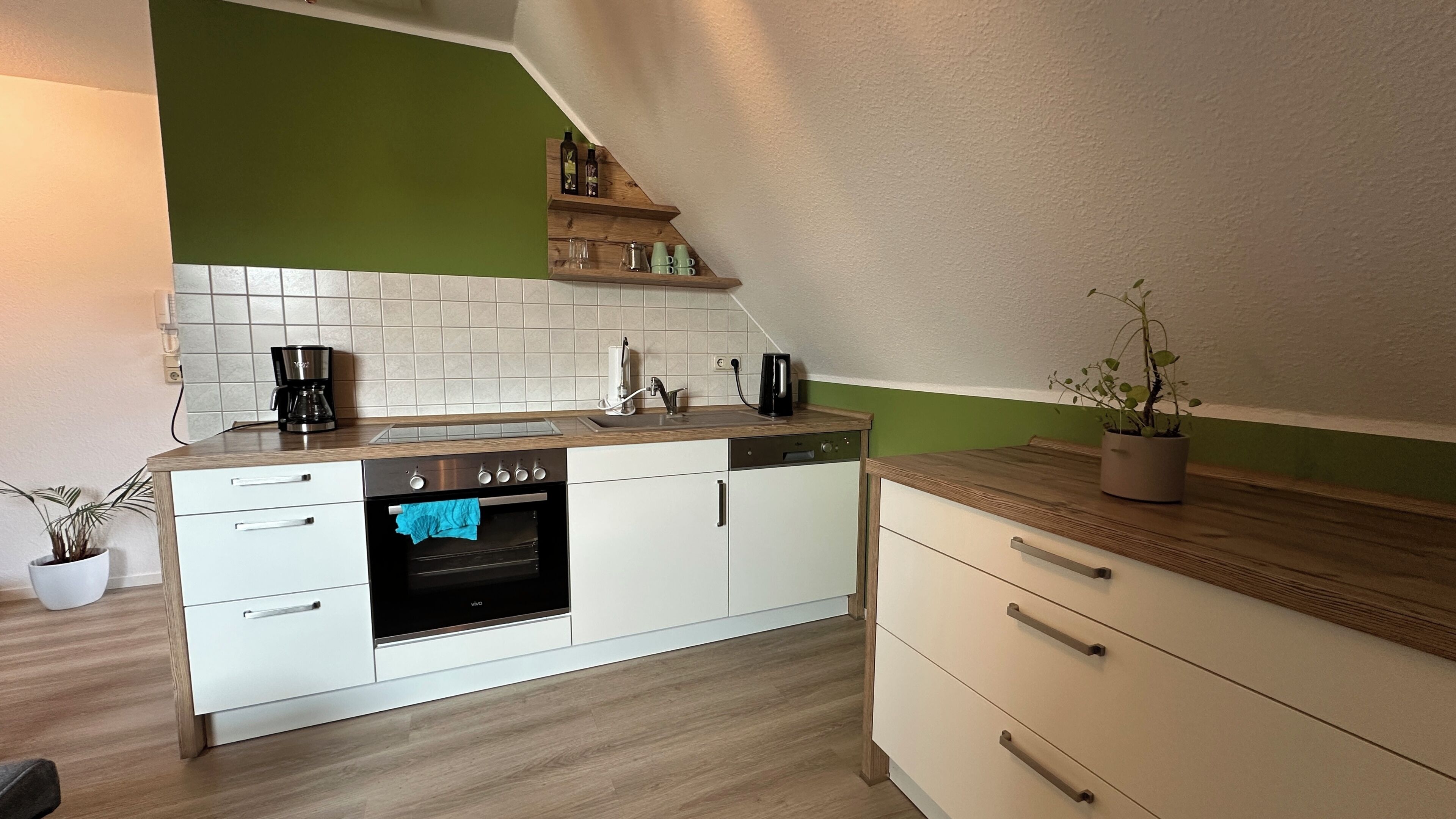 Eine Küche mit weißen Schränken, einem eingebauten Backofen, einer Kaffeemaschine und einem Regal mit Flaschen und Gläsern.