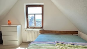A bedroom with a sloped ceiling, a window, a bed, a dresser, and a radiator. - Maisonette-Wohnung am Markt  zentral in Wolkenstein, für 4 Gäste (Wolkenstein)