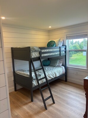 A bunk bed with a ladder, white walls, and a window with a view of greenery. - Rustic Bay Vacation Home (Lot 65)