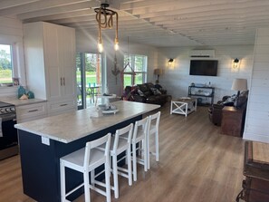 A modern kitchen with a central island, white cabinetry, and a dining area with a sofa and coffee table. - Rustic Bay Vacation Home (Lot 65)