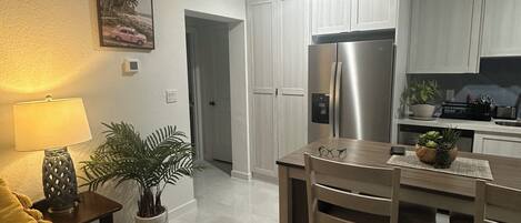 A modern kitchen with white cabinets, a stainless steel refrigerator, and a dining area with a wooden table and chairs.