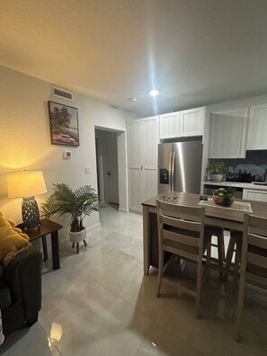 Een moderne keuken met witte kasten, een roestvrijstalen koelkast en een eethoek met een houten tafel en stoelen.