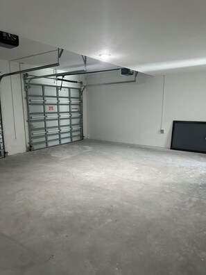 A garage with a metal gate, concrete floor, and a ceiling light. - Elegant and cozy apartment on Hoestead (Homestead)