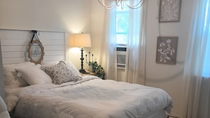 A bedroom with a large bed, a bedside table with a lamp, a chair, and a chandelier. - Tranquil 1-bedroom cottage in the pines in Mount Enterprise (Mount Enterprise)